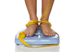 A person steps on a scale. Their legs and feet are wrapped in measuring tape.