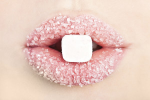 Someone's lips are covered in sugar. They hold a sugar cube.