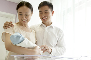 A mom and dad hold their newborn baby in their arms and smile.