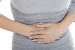 A woman holds her stomach and appears bloated.