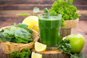 A healthy green smoothie is shown next to lemons, spinach, broccoli and a green apple.