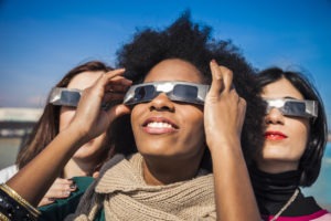 Three people wear glasses with a special filter, ISO12312-2, as they look at the solar eclipse.