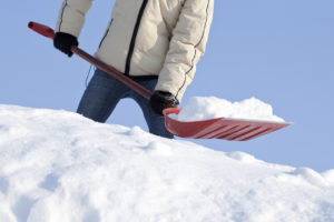 A person shovels snow with a red shovel.