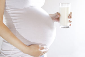 A pregnant woman holds a full glass of milk.