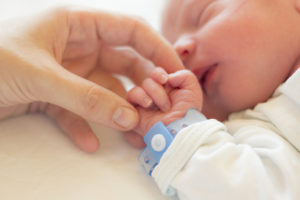 A newborn baby sleeps while holding onto a hand.
