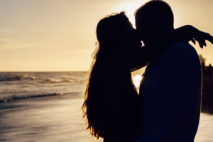 A man and woman kissing each other at a beach.