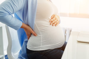 A pregnant woman holds her stomach. She appears uncomfortable.