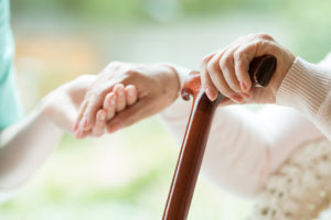 A caregiver holds an elderly woman's hand.