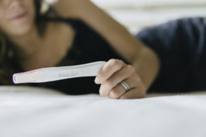 A woman lies in bed and looks at a pregnancy test.