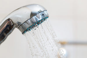A showerhead is in focus. Water is coming out of the showerhead.