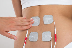 The TENS unit is places on a woman's back. The TENS unit works by sending electrical currents to electrodes on the body.