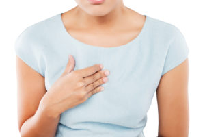 A woman places her hand over her heart and appears uncomfortable. She wears a blue T-shirt.
