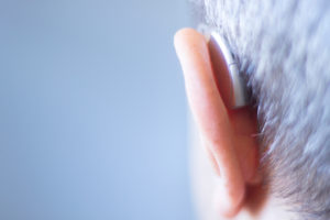 A hearing aid is shown in an elderly person's ear.