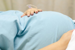 A pregnant woman lies in a hospital bed and holds onto her belly as she prepares for labor.