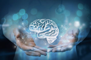 A person reaches their hands out toward a hologram of a brain. 