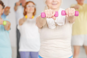 A group of people participate in a fitness class together. They all are using dumbbell weights.