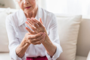 An elderly woman holds her wrist and appears to be in pain.