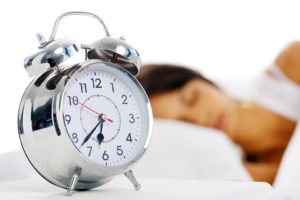 An alarm clock is shown next to a person sleeping.