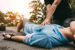 A person performs CPR on a person who lies down on the street.