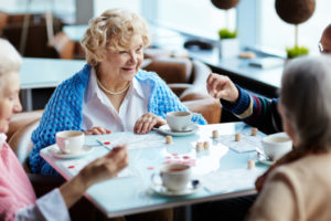 A group of elderly adults drink coffee and play a game at a restaurant.