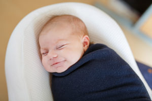 A baby is shown tucked in a dark blue blanket, sleeping.