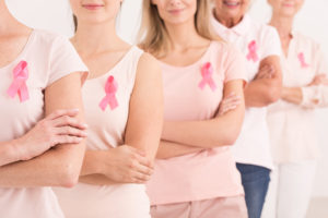 A group of women wearing pink breast cancer ribbons on their shirts are shown.