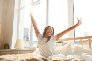 A woman wakes up and stretches her arms in the air, in bed.