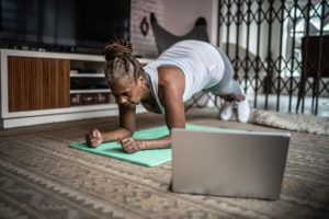 A person exercises on a yoga mat inside her home. She appears to be holding a plank.